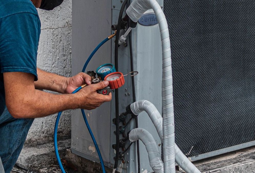 Technician repairing an air conditioner unit outdoors, wearing a facemask and using a manifold gauge.
