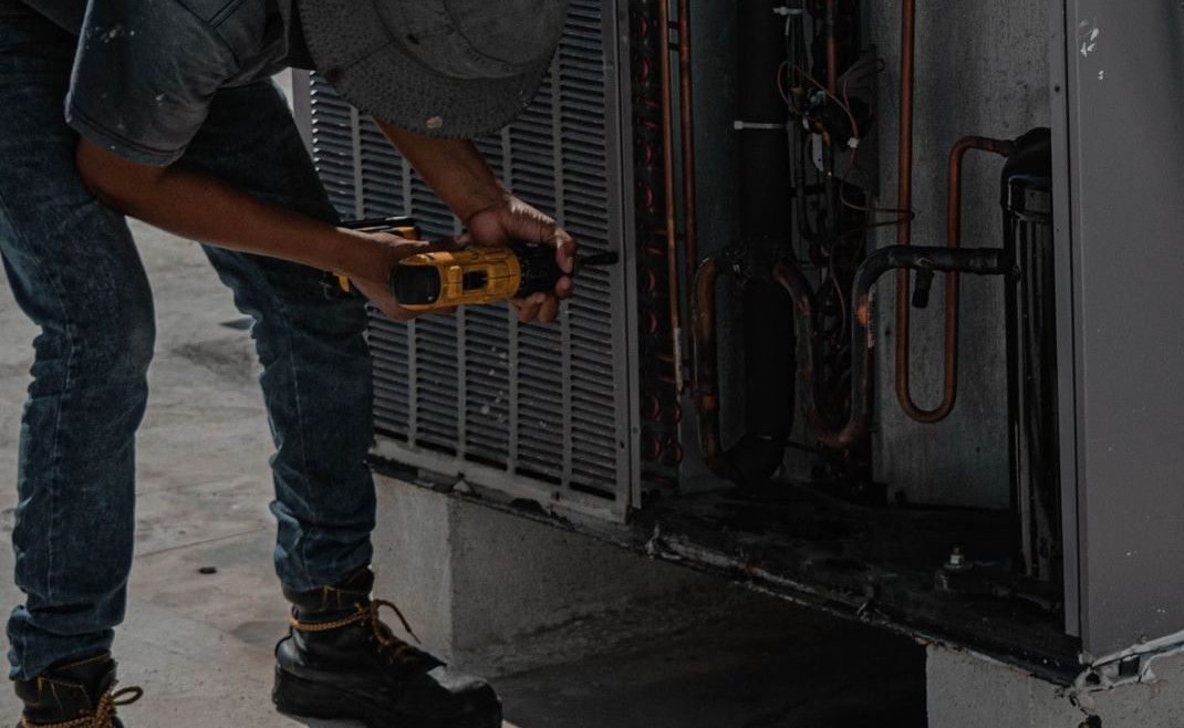 A technician is repairing an air conditioning unit on a rooftop, demonstrating skilled manual work.